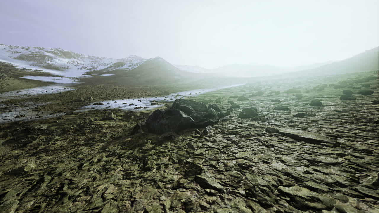 Expansive rocky landscape under a pale sky with distant snow covered peaks