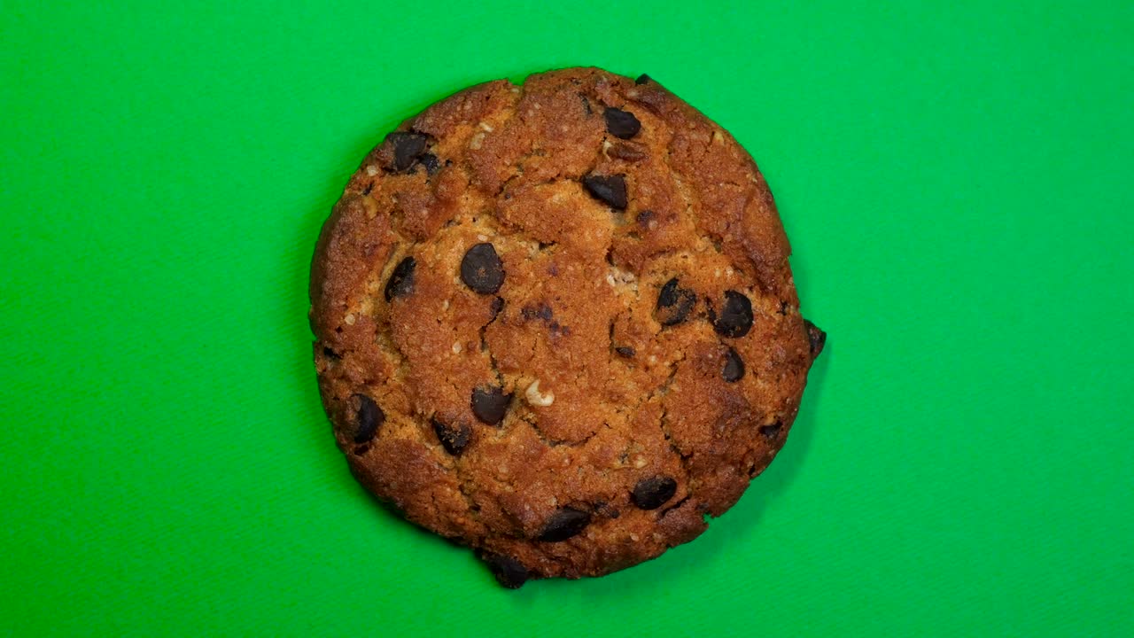 Chocolate chip cookie close-up, macro shot, slowly spinning on a rotating green background.