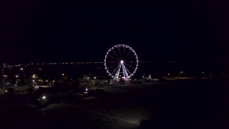 illuminated ferris wheel against sky at night in rimini, italy - aerial shot