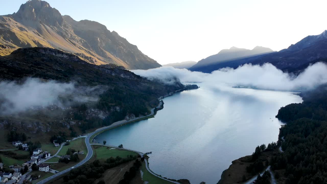 Un sorvolo aereo all'alba sul Lago di Sils a Maloja, Svizzera, con vista sulle cime dell'Engadina e nuvole che si muovono sull'acqua