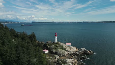 Vista-Aérea-Inclinando-Hacia-Abajo-El-Faro-De-Point-Atkinson-En-El-Parque-Del-Faro-Cerca-De-La-Ciudad-De-Vancouver-En-Un-Día-Soleado-Con-Algunas-Nubes-En-Columbia-Británica,-Canadá