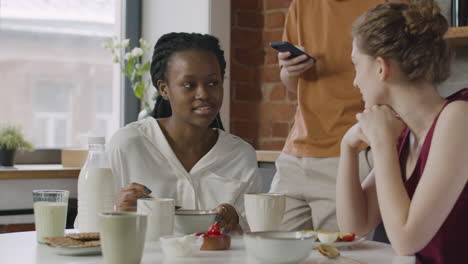 two  female roommates having breakfast and talking together in the kitchen at home