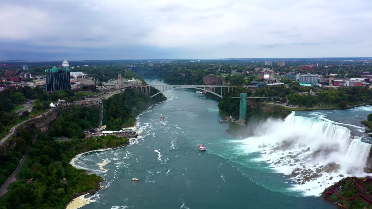 Aerial view of mist rising from Niagara Falls as city skyline emerges in the background, dolly to bridge
