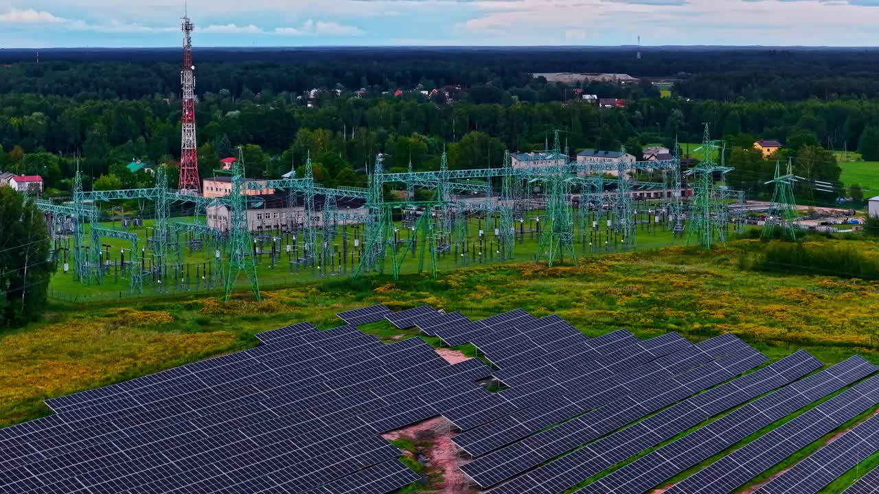 Luftfoto af et solcelleanlæg ved siden af en stor, elektrisk transformerstation, der viser vedvarende energi, som føres ind i den regionale strøminfrastruktur omgivet af et grønt landskab