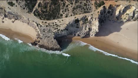 Beeindruckender-Mareta-Strand-Mit-Klippen-In-Südportugal,-Drohnenaufnahme-Von-Oben,-Surfer-Bei-Sonnigem-Wetter