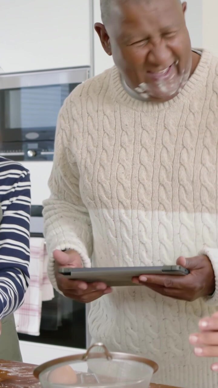 Vertical video: Reading tablet recipe, man with flour and woman in apron mixing bowl in kitchen