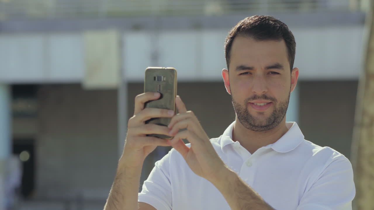 hombre barbudo sonriente sosteniendo un teléfono inteligente y mirando a la cámara.