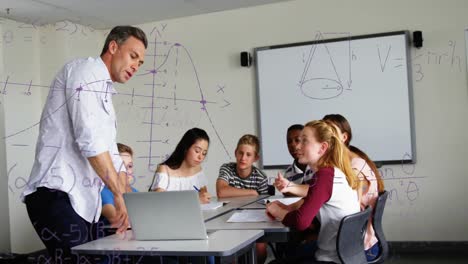 Mathematical-equations-floating-against-male-teacher-using-laptop-to-teach-students