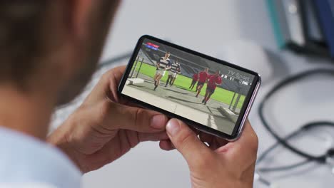 Composite-of-male-doctor-watching-rugby-match-on-smartphone