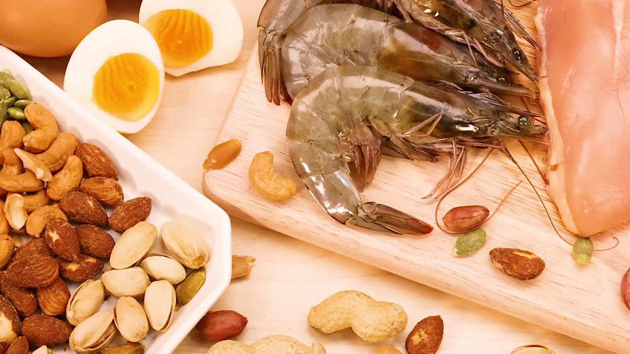 A selection of nuts, shrimp, and chicken breast arranged on a wooden board with boiled eggs.