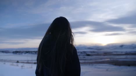 Parallax-shot-young-woman-looking-out-over-snowy-winter-landscape-at-dawn