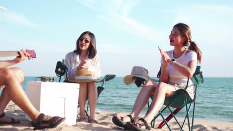 해변에서 음악과 함께 즐기는 행복한 젊은이, 기타를 연주하는 젊은이, 친구들이 박수를 치고 웃는 것처럼, 여름 휴가, 휴가 동안 해변 피크닉에서 재미있게 즐기고.