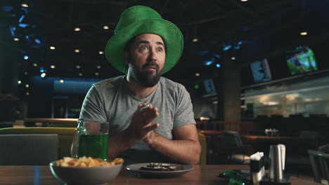 Hombre-Con-Sombrero-Irlandés-Viendo-Un-Partido-De-Fútbol-En-La-Televisión,-Reaccionando-Emocionado