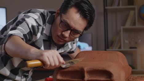 close up of asian man automotive designer works on the sculpture of car clay using spatula to smooth out the surface and create details in the design in the studio