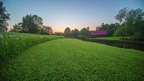 Ein-Goldener-Sonnenuntergang-An-Einem-Ländlichen-Fluss-Mit-Löwenzahn-Und-Wildblumen-Auf-Einem-Feld-–-Zeitraffer