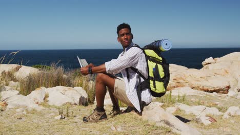 African-american-man-hiking-sitting-holding-a-map-in-coastal-countryside