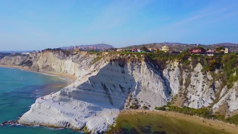 Toma-Aérea-De-Los-Acantilados-Blancos-Sicilianos-De-Scala-Dei-Turchi-Que-Se-Elevan-Desde-La-Playa-De-Arena-Dorada-Debajo