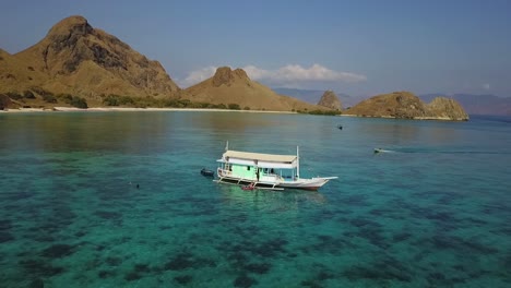 aerial of a traditional liveaboard in indonesia with people waving in ocean, padar island