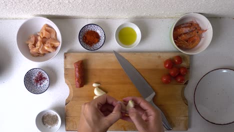 male chef using back of knife to peel garlic cloves on wooden cutting board