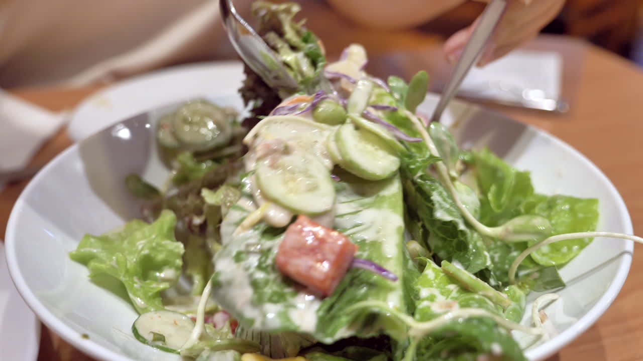 Mixing a bowlful of vegetable salad and mayo dressing, using a spoon and fork, inside a restaurant in Bangkok, Thailand