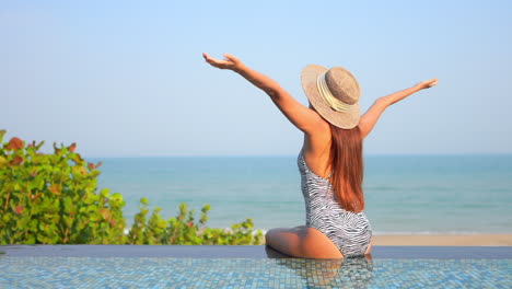 Young-Adult-Woman-in-Bathing-Suit-Spreads-Arms-at-Swimming-Pool-Side