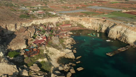 Pueblo-Popeye-En-La-Bahía-Ancla,-Isla-Gozo,-Malta-Tomada-Desde-Arriba-Con-Vistas-Al-Pueblo-A-La-Luz-Del-Atardecer