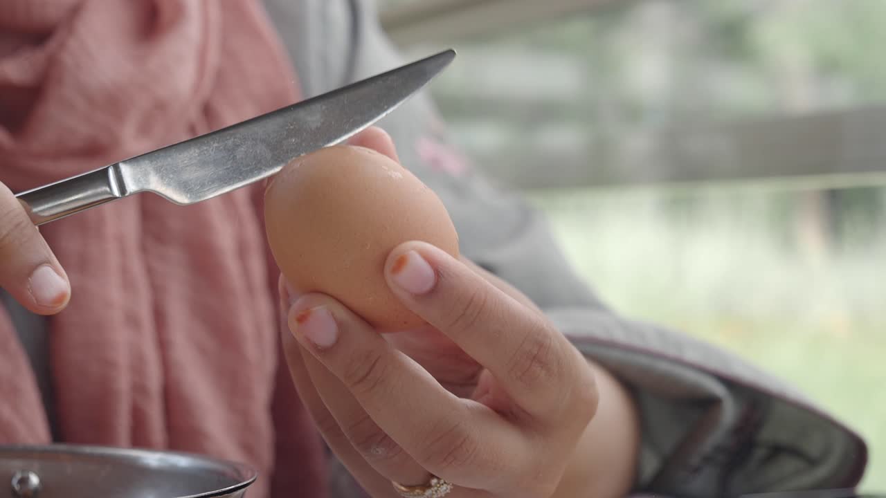 A person peeling a hard boiled egg with a knife