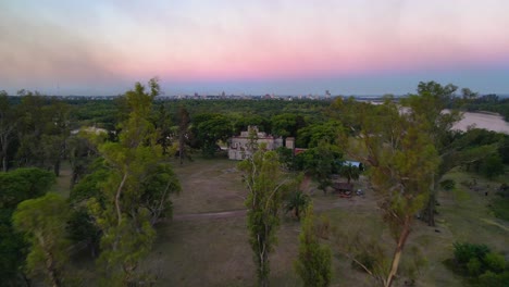 disparo de drone volando hacia la estancia santa cándida en entre ríos, argentina al atardecer con la ciudad de concepción del uruguay al fondo
