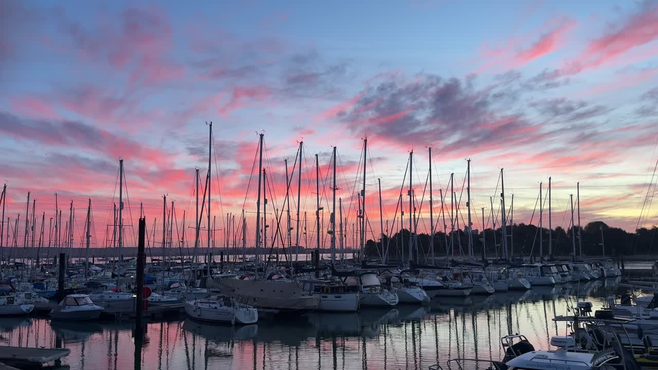 A wide shot captures numerous sailboats docked in Gosport Marina under a stunning pink and blue sunset sky with reflections on the calm water