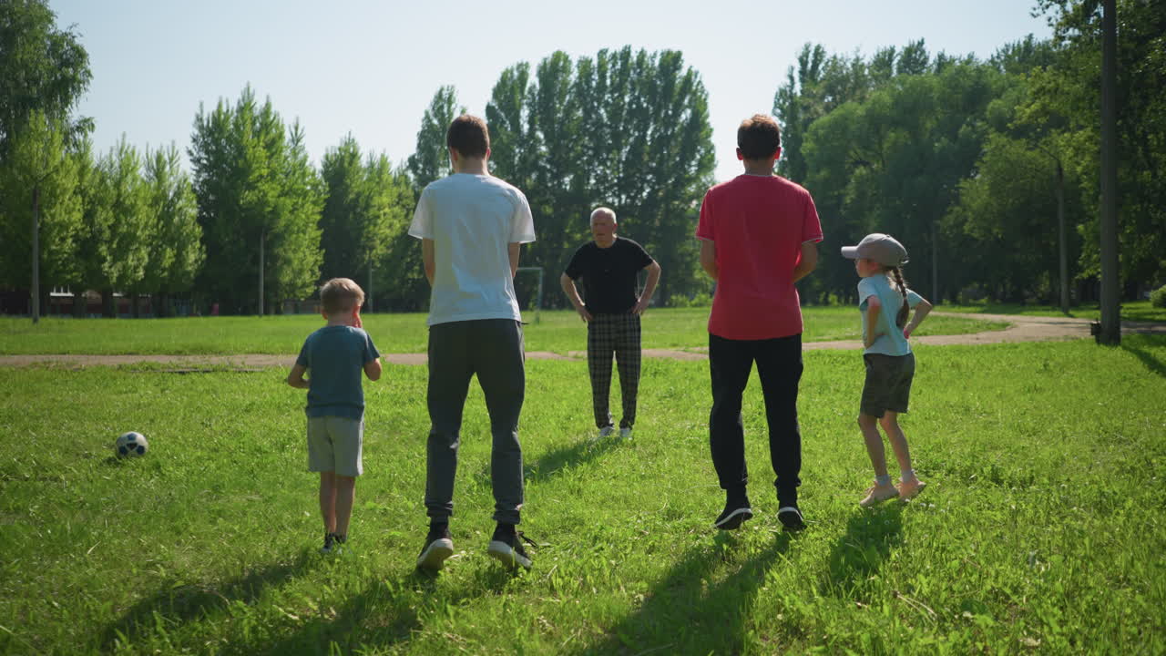 한 가족이 야외에서 놀고 있는데, 할아버지는 손자들을 이끌고, 손자들도 함께 뛰어다니고, 한 아이가 공을 들고, 아버지가 다른 공을 던집니다.