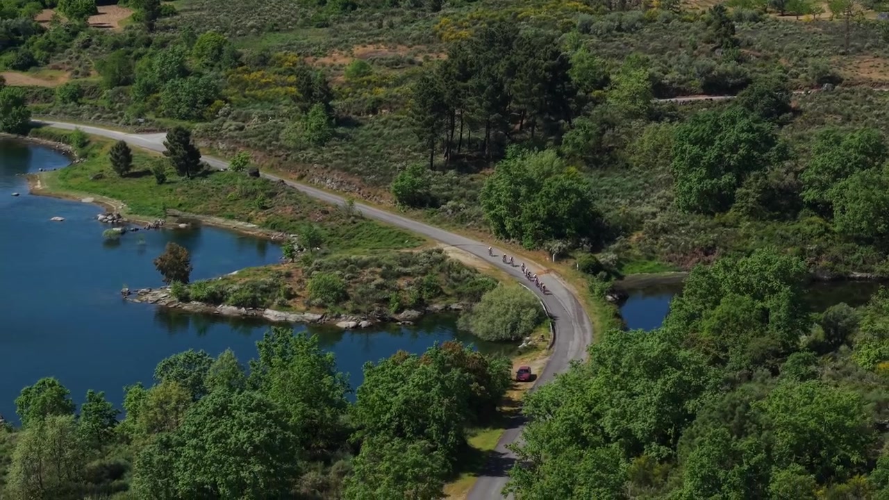 Ciclisti in gara su una strada rurale lungo la riva rocciosa del bacino del Douro con un versante terrazzato e alberi