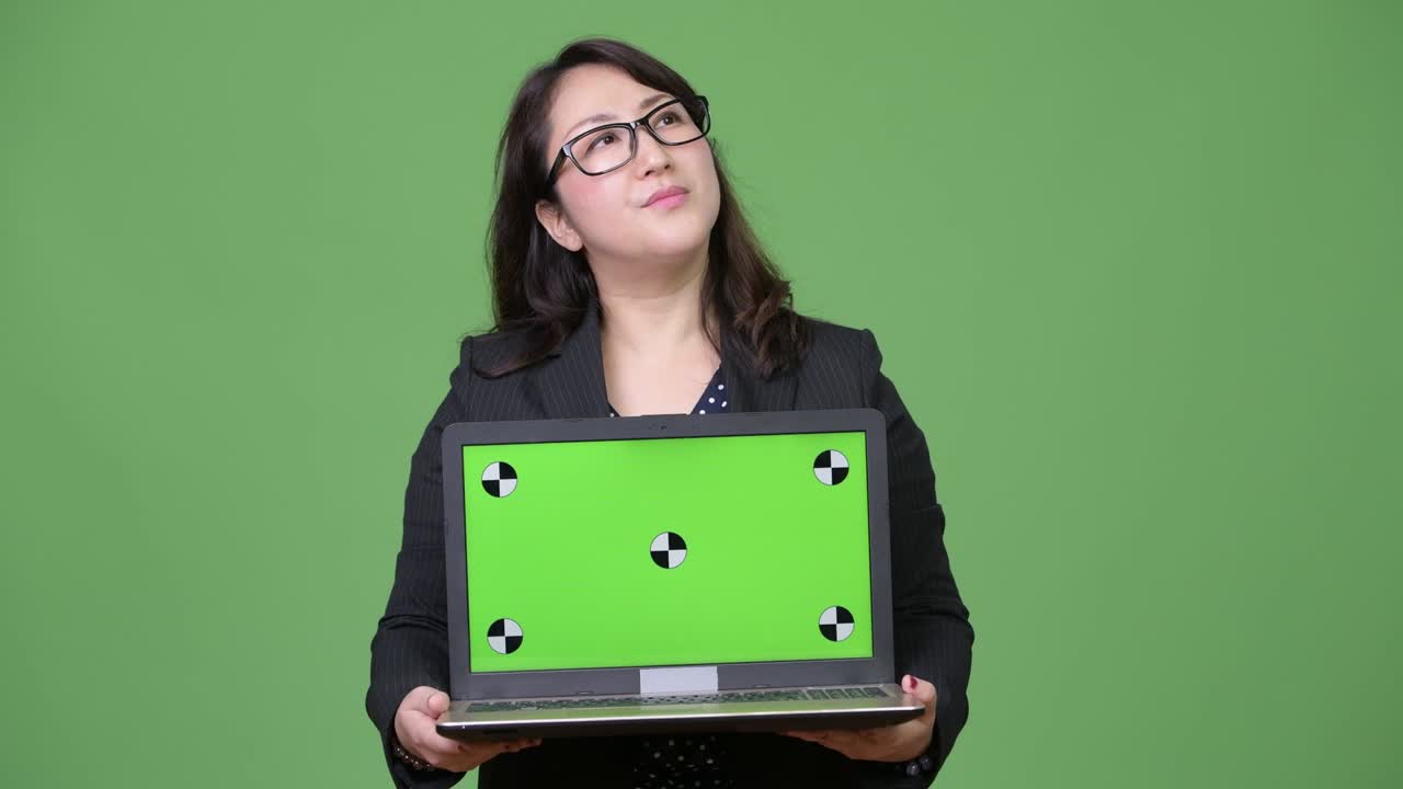 una hermosa mujer de negocios asiática madura mostrando una computadora portátil contra un fondo verde
