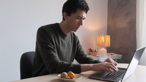 Mixed-Asian-man-typing-on-his-laptop-computer-while-working-from-home