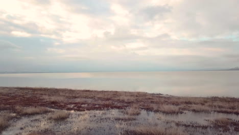 gliding above a marshy area towards a vast lake with sky reflecting off the water