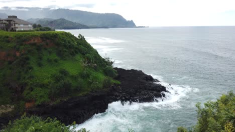 4k hawaii kauai short truck left to right from greenery to reveal waves crashing on rocky shore with mountains in distance