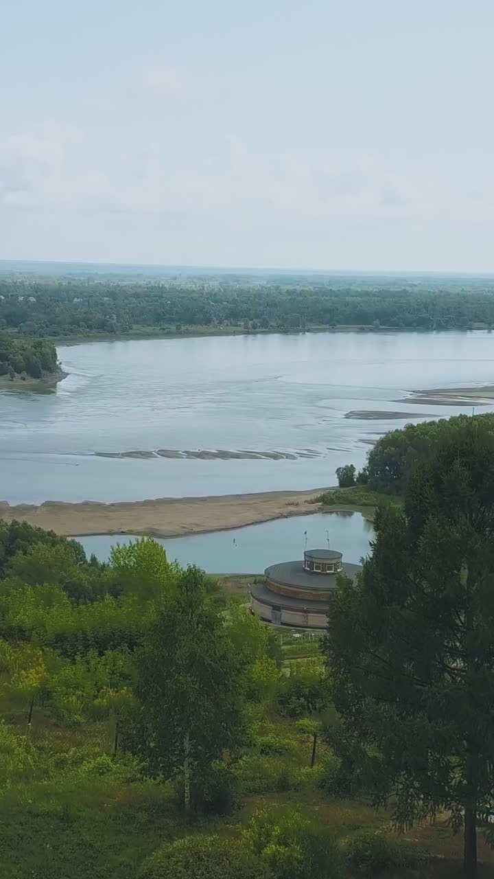 young newlywed couple sits on bench near fir tree on hill against picturesque wide river on autumn day aerial panorama