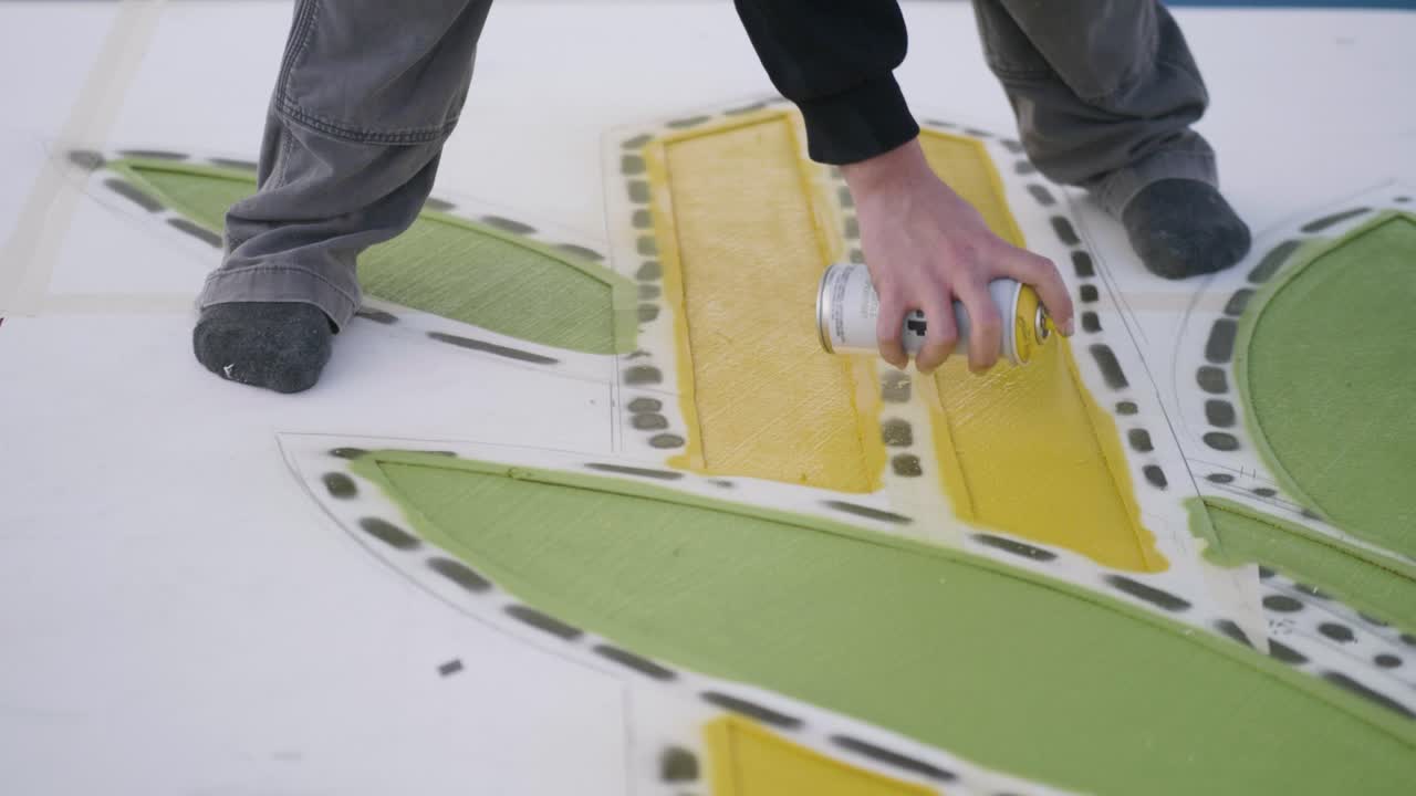 Barefoot artist using spray paint to do coloring job, close up