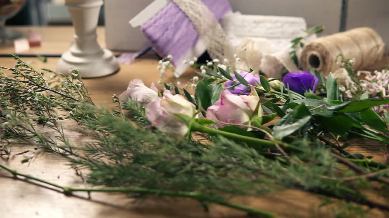 Slow camera movement showing wooden table with flowers, scissors, tapes, decorating paper and other tools for bouquet