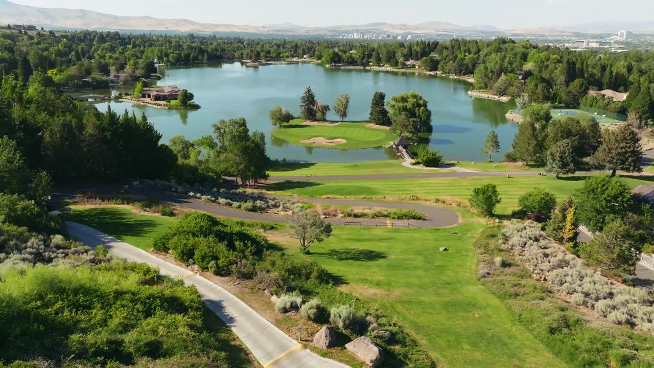 Pengambilan gambar orbit udara dua mobil golf yang melaju di jalur kereta menuju danau indah dengan lapangan hijau pulau di kejauhan.