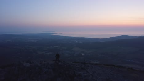 aerial - flyover silhouette of a man standing on top of the mountain and watching beautiful sunrise