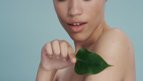 close-up-portrait-sexy-young-woman-touching-body-with-leaf-caressing-smooth-healthy-skin-complexion-enjoying-playful-natural-beauty-on-blue-background-skincare-concept