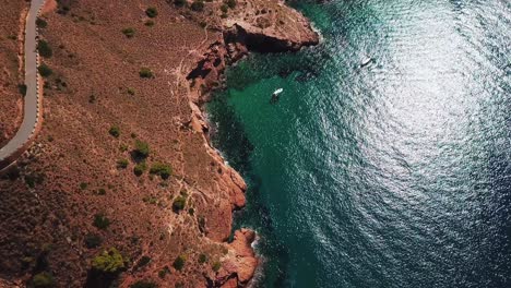 Aerial-downward-slow-motion-view-of-two-white-boats-sailing-in-calm-and-silent-ocean-with-shining-water-due-to-sunlight-surrounded-by-mountain-in-Benidorm-in-Spain