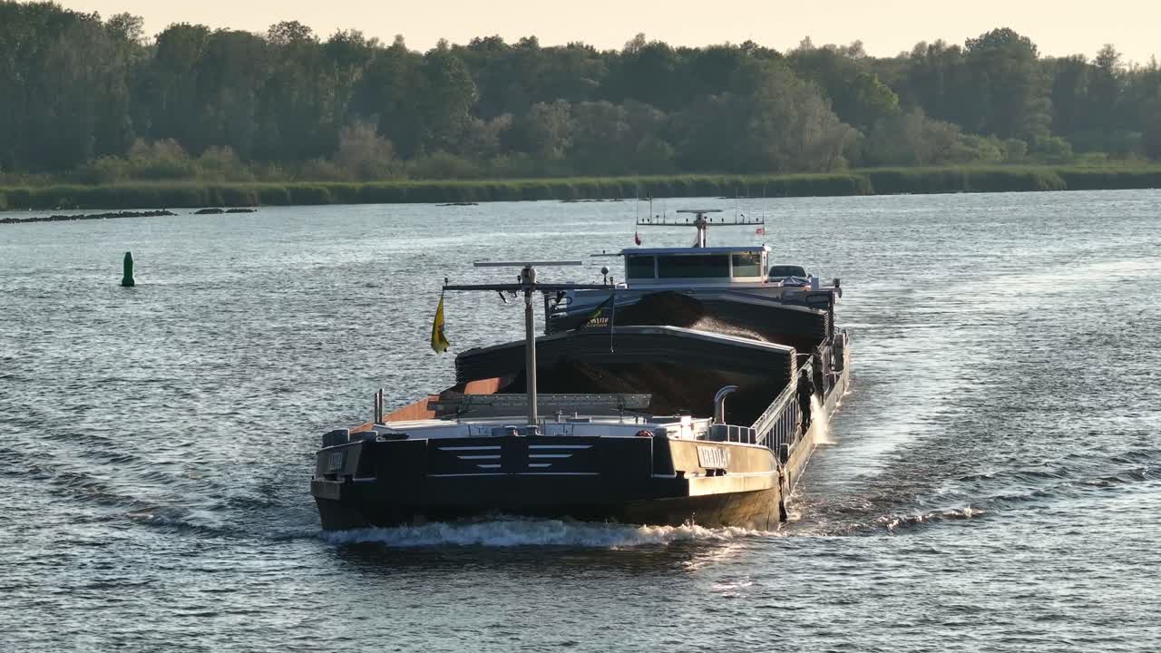 Dutch freighter ship Kedia transports coal on river at golden hour, aerial pan
