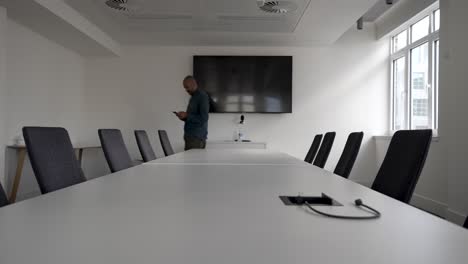 Impatient-businessman-looking-on-smartphone-waiting-for-guests-in-meeting-room