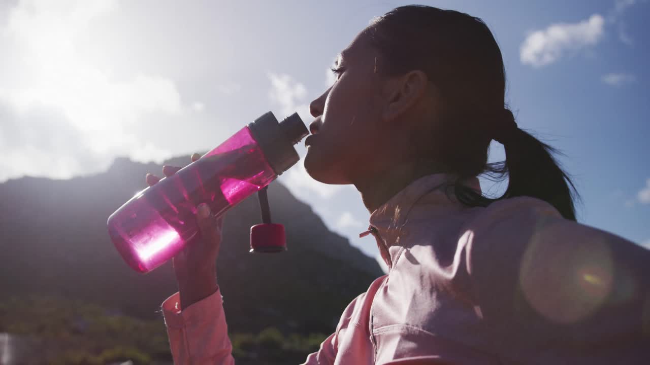 mujer afroamericana bebiendo agua de la botella mientras caminaba en las montañas