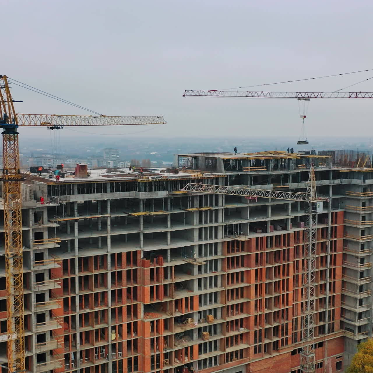 New construction in the city center. Wide high-rise building under construction outdoors. Aerial view. Camera moving around.