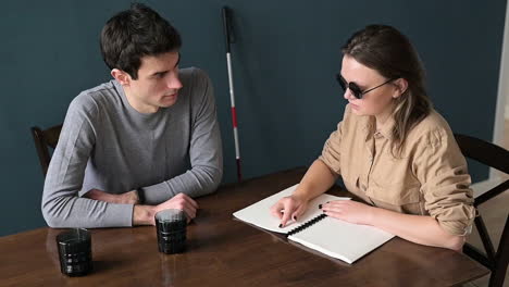 top view of man and blind woman in sunglasses sitting at table at home talking