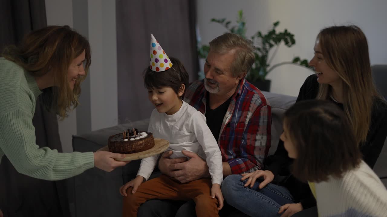 작은 소년은 꿈의 불을 불어넣고 행복한 가족의 원에서 케이크를 니다.