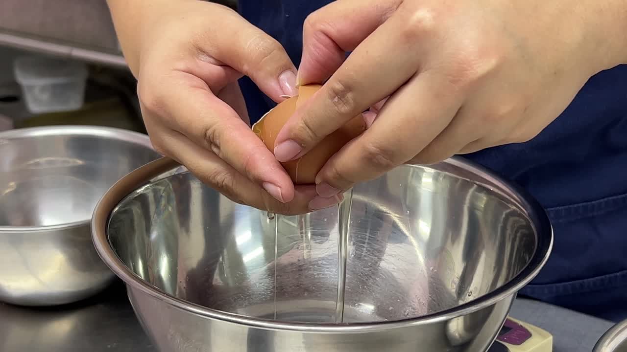 pastelero rompiendo el huevo, separando la clara de huevo y la yema de huevo en diferentes recipientes de mezcla de acero inoxidable, ambiente de panadería de cocina comercial