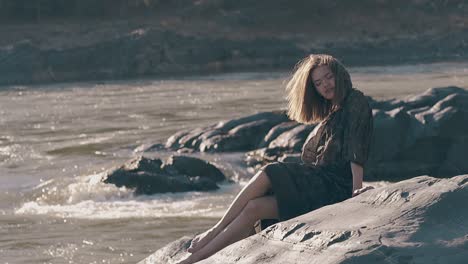 barefoot lady in tight dress poses on rocky river bank